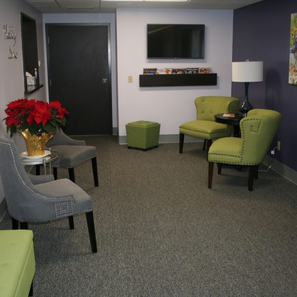 picture of our waiting room with green and grey chairs and a television