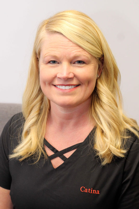 Blonde woman with long hair smiling, wearing black scrubs