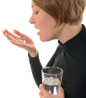 woman about to take two pills that are in her palm and holding a glass of water in her other hand