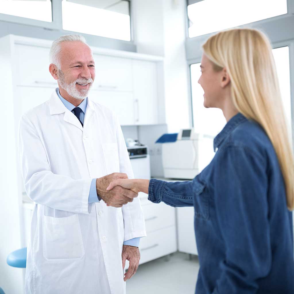 Image of an older-looking dentist, smiling and shaking a young woman's hand