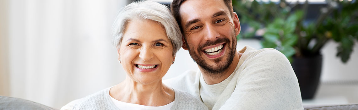 an older woman smiles as her son hugs her while smiling