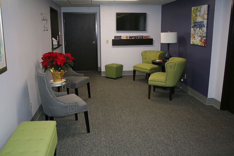 picture of our front office waiting room with green and grey chairs and a television